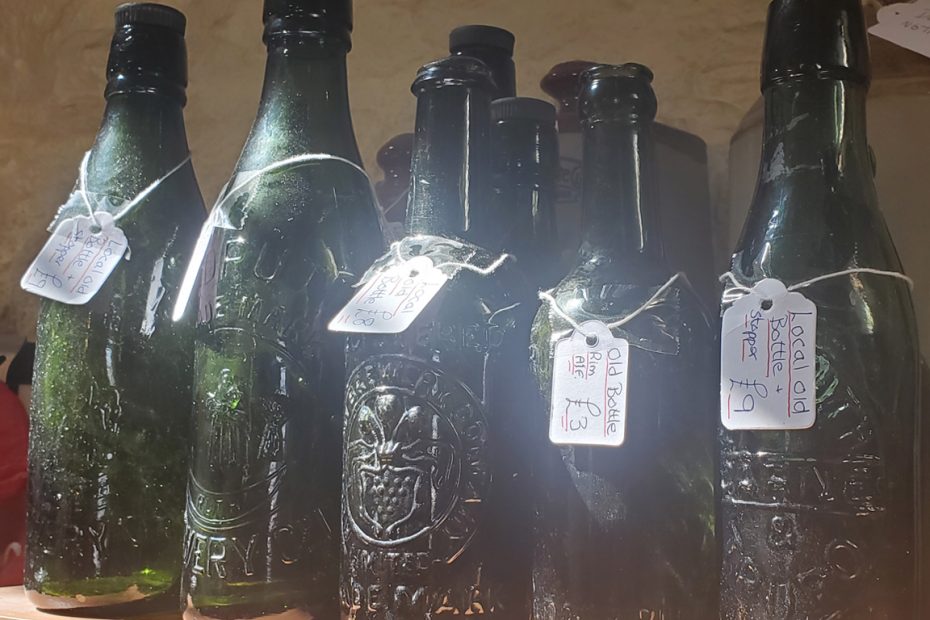 Photograph showing a row of dark green glass bottles from local breweries