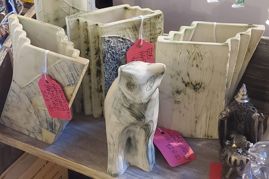 Photograph of a shelf of Carn pottery pieces including geometric vases and a cat sculpture. White with smoky black detailing.