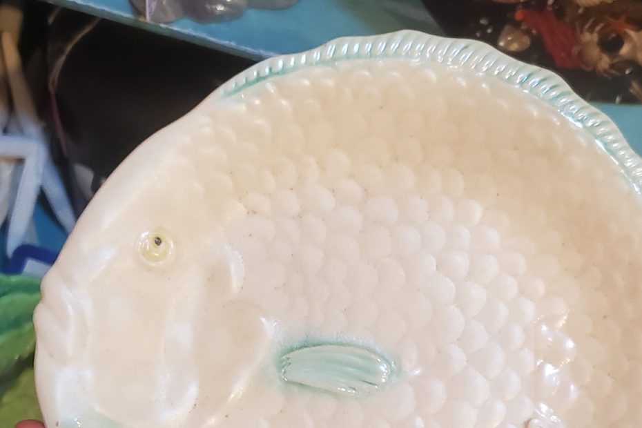 White, round fish plate with a brilliant expression with an upturned mouth and little fin.